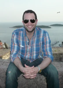 A man wearing sunglasses sitting at a scenic coastal viewpoint