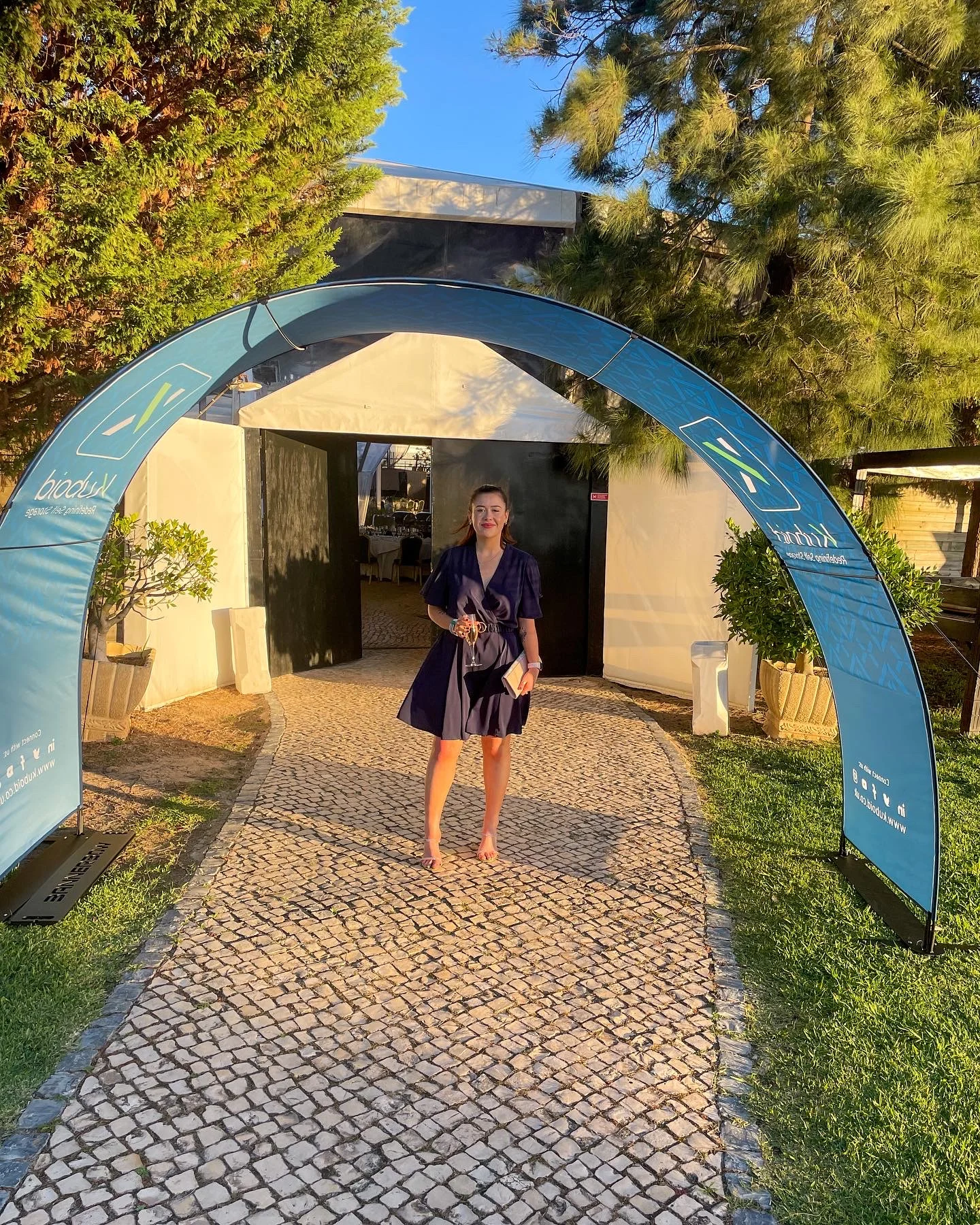 Simone standing under a branded Kuboid arch at an outdoor event