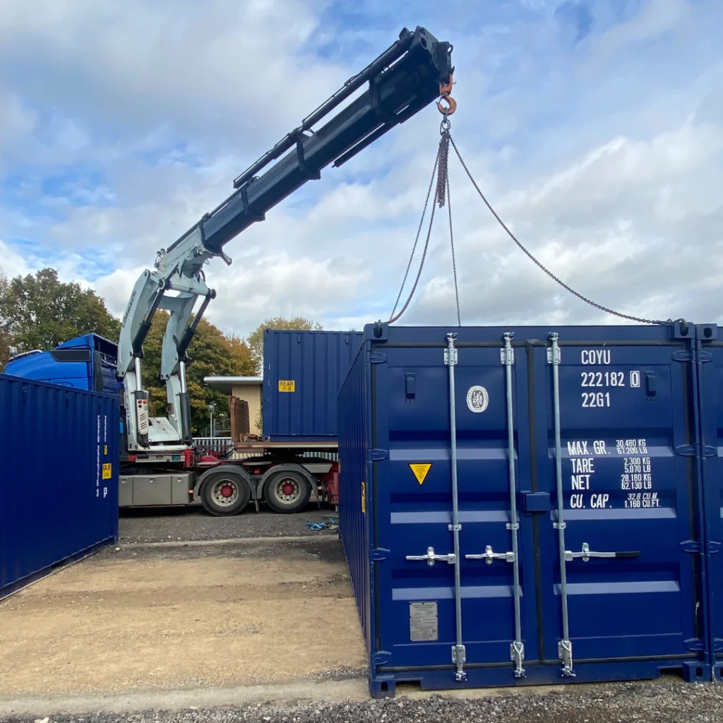 A blue shipping container being lifted by a crane truck at a container storage yard